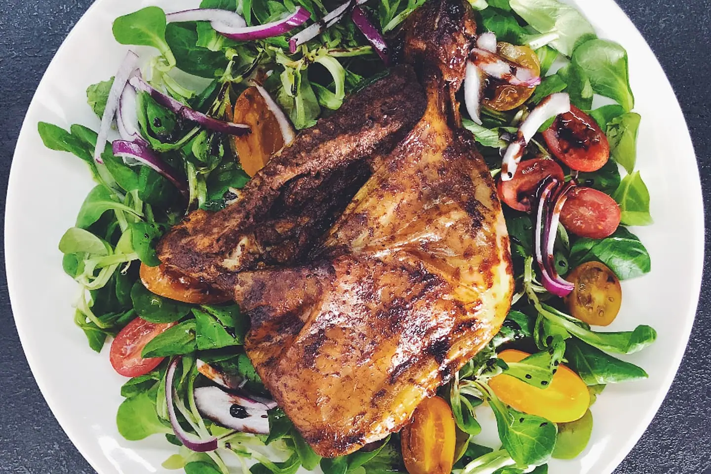 Gegrilltes Hähnchen auf buntem Salat mit Tomaten und roten Zwiebeln